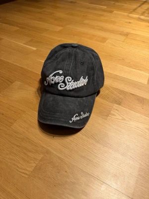 Grå keps från Acne Studios - Säljer en grå keps från Acne Studios med broderad vit logga både framtill och på skärmen. Klassisk böjd skärm och justerbar rem bak. Tillverkad i mjuk bomull med tvättad look som ger en avslappnad vibe. Säljer för att jag inte passar i keps