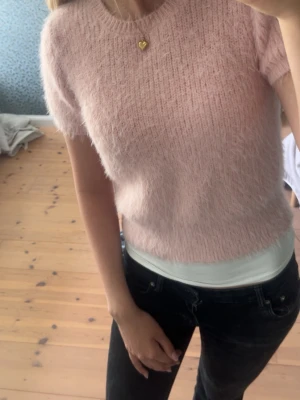 Ljusrosa stickad tröja från Zara - Mjuk och fluffig ljusrosa stickad tröja från Zara med korta ärmar och rund halsringning. Tröjan har en ribbstickad kant vid halsen och är tillverkad i ett luddigt material som ger en cozy känsla. Perfekt för att addera lite färg till din outfit.