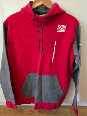 Nike NFL New York Giants Hoodie XL – Team Apparel 🔥 - Snygg hoodie från Nike i rött och grått med vit NY-logga på bröstet och vit Nike Swoosh på ärmen. Huva med dragsko, magficka och en vit dragkedjeficka på bröstet. Perfekt för en sportig och avslappnad stil.