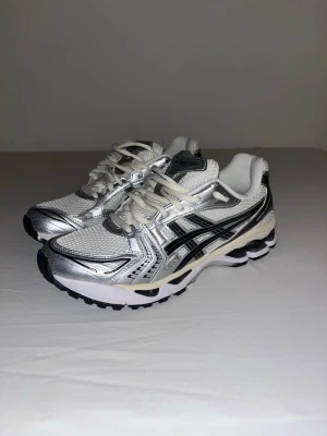 ASICS silvriga sneakers med mesh - Snygga sneakers från ASICS i silver och vitt med svarta detaljer. Ovandelen är i mesh och syntetmaterial för en sportig vibe. Klassisk snörning och bekväm sula som passar perfekt till streetwear eller en chill outfit.
