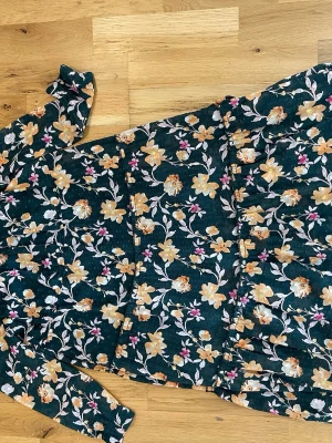 Blommig långklänning med långa ärmar stl 122 cm fint skick - Mörkgrön långklänning med blommigt mönster i gult, vitt och rosa. Klänningen har långa ärmar och markerad midja. Perfekt för dig som gillar romantisk och färgglad stil.