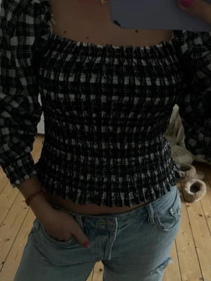 Svartvit rutig smockad blus - Trendig svartvit rutig blus med smockad kropp och puffiga långärmar😍Toppen har en croppad passform och fyrkantig ringning, vilket ger en cool och modern vibe. Perfekt att styla med jeans för en avslappnad look⭐️ Skriv privat för mer bilder eller prisförslag🙌🙌