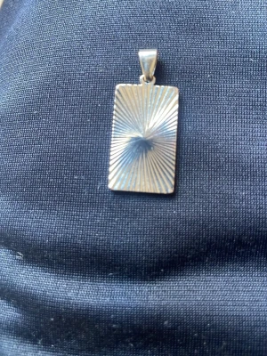 Rektangulärt silverfärgat halsband - Snyggt halsband med ett rektangulärt hänge i silverfärg. Hänget har ett coolt solstrålemönster på framsidan och en slät baksida. Perfekt för dig som gillar stilrena och moderna accessoarer. Materialet ser ut att vara metall.