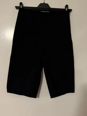 Svarta bermudashorts från H&M - Stilrena svarta bermudashorts från H&M med rak passform och längre ben. Perfekta för en clean och enkel look. Shortsen har en klassisk design utan synliga detaljer och är tillverkade i ett mjukt material som känns bekvämt mot huden.
