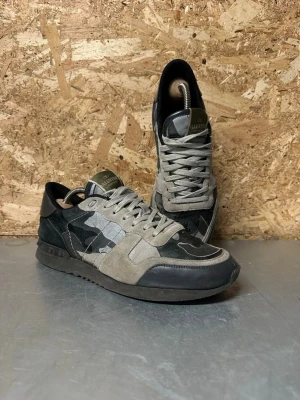 Valentino Rockrunners - Snygga sneakers från Valentino med grått och svart kamouflagemönster, detaljer i mocka och läder samt svarta och gråa partier. Skorna har klassisk låg profil och vita snören. Perfekta för dig som vill sticka ut med stilrena detaljer.