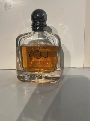 Emporio Armani Stronger With You parfym - Emporio Armani Stronger With You är en elegant parfym i en genomskinlig glasflaska med rundade former och svart rund kork. 100ml flaska så ungefär 60-70 ml kvar. Doften har en varm bärnstensfärgad vätska och flaskan har märkets logga tryckt framtill.