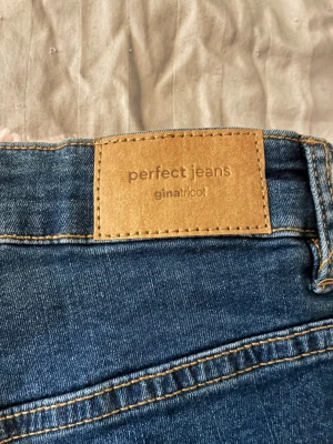 Blå jeansshorts från Gina Tricot - Snygga blå jeansshorts från Gina Tricot med klassisk femficksdesign och uppvikta benslut. Perfekta för sommaren och enkla att matcha med olika toppar. Hög midja och skön passform.