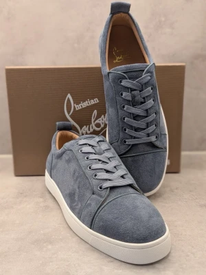 Blå mockasneakers från Louboutin - Snygga blå sneakers i mocka från Christian Louboutin med klassisk vit sula och den ikoniska röda undersidan. Skorna har rund tå, tonade skosnören och diskreta sömdetaljer. Perfekta för dig som vill ha en stilren och lyxig look.