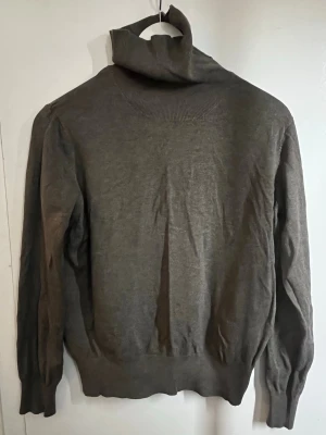 Grå/brun polotröja  - Mjuk och stilren grå/brun polotröja med lång ärm och ribbade muddar vid ärmslut och nederkant. Perfekt för lager på lager och enkel att matcha med olika outfits. Polokragen ger en extra mysig känsla och tröjan har en klassisk passform.