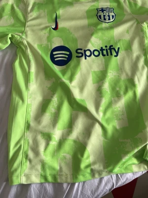 FC Barcelona neon grön matchtröja - Säljer en neon grön FC Barcelona matchtröja år 24/25. Likadan tröja som Yamal hade på sig mot Inter. Den e från Nike med klubbmärke, Nike-logga och Spotify-tryck på bröstet. UNHCR-logga på ryggen. Tröjan har korta ärmar och är tillverkad i ett lätt och ventilerande material, perfekt för fotbollsträning eller match eller supporter. Lite remsar som gått upp lite. Bild 4.