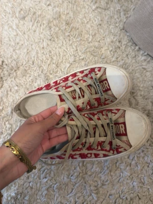 Röda Christian Dior sneakers - Snygga sneakers från Christian Dior med röd och vit monogramdesign. Skorna har lite smutsiga sulor, beige snörning och detaljer med logotypen på snörningen. använt skick men skiiit snygga i 39. 