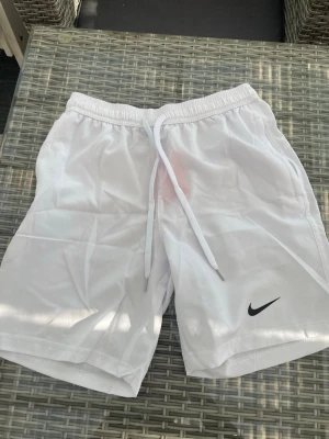 Vita Nike shorts - Säljer ett par vita shorts från Nike. De är från Nike och knappt använda size S
