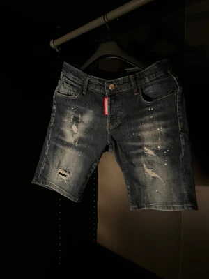 DESQUARED2 jeansshorts med slitningar - Snygga mörkblå jeansshorts från DSQUARED2 med slitna detaljer och coola färgstänk. Klassisk femficksmodell med knapp och dragkedja. Perfekta för en avslappnad streetstil.