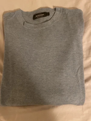 Ljusblå stickad tröja Dressmann - En stilren ljusblå stickad tröja från Dressmann. Tröjan har rund halsringning, långa ärmar och ribbade muddar vid ärmslut och nederkant. Perfekt att matcha med jeans eller chinos för en clean look. Kan komma ner i pris vid snabb affär