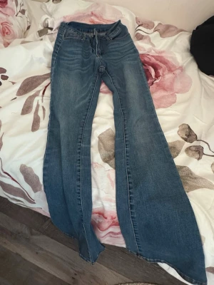 Blå utsvängda jeans med hög midja - Säljer ett par blå jeans med riktigt breda utsvängda ben och hög midja. Klassisk femficksmodell i denim med dragkedja och knapp framtill. Perfekta för dig som gillar retrostil och vill sticka ut med en unik siluett.