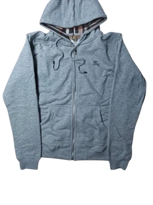 Grå zip-hoodie från Burberry - Snygg grå hoodie med dragkedja från Burberry. Klassisk huva med dragsko och kängurufickor framtill. Tillverkad i mjuk bomull med en touch av elastan. Fodret i huvan har det ikoniska Burberry-rutiga mönstret.