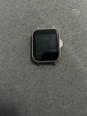 Denver smartklocka silverfärgad - Snygg smartklocka från Denver med fyrkantig svart display och silverfärgad ram i metall. Klockan har pulsmätare på baksidan och en rund knapp på sidan. Perfekt för dig som vill ha koll på hälsa och notiser direkt på handleden.och laddare kommer med 