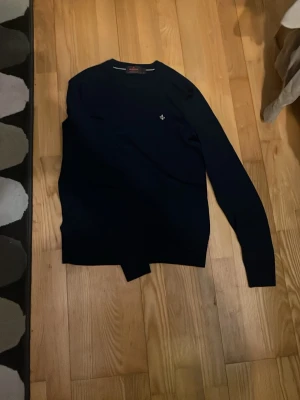 Mörkblå tröja från Morris - Mörkblå tröja från Morris i klassisk modell med rund halsringning och diskret broderad logga på bröstet. Tillverkad i 100% bomull, perfekt för en stilren och enkel look.