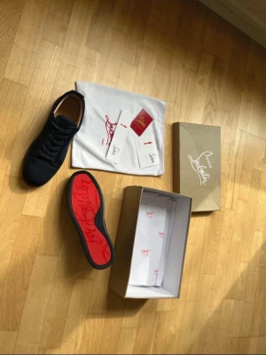 Svarta Christian Louboutin sneakers - PRIS GÅR ATT DISKUTERA. Snygga svarta sneakers från Christian Louboutin med klassisk röd sula och diskret logga. Skorna har en låg profil och är tillverkade i mocka med svarta skosnören. Perfekt för dig som vill sticka ut med exklusiva detaljer.