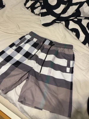 Rutig shorts från Burberry - Snygga shorts från Burberry med klassiskt rutigt mönster i svart, vitt, grått och beige. Modellen har elastisk midja med snörning och sidofickor. Perfekta för sommaren och ger en trendig vibe till din outfit.