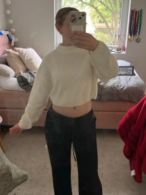 Vit cropped stickad tröja - Säljer en vit stickad tröja med cropped passform och ribbad struktur. Tröjan har långa ärmar och en hög, ribbad halsringning. Perfekt för att skapa en trendig och avslappnad look. Materialet är mjukt och bekvämt.