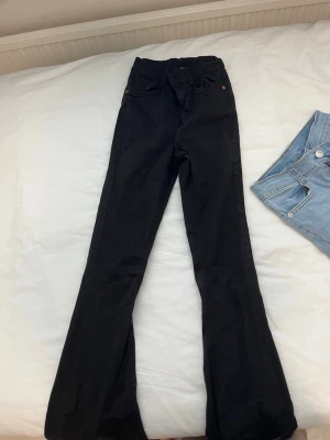 Svarta utsvängda jeans - Snygga svarta jeans med utsvängda ben och hög midja. Perfekta för dig som gillar en trendig och bekväm stil. Klassisk femficksmodell och stretchigt material som sitter skönt hela dagen.
