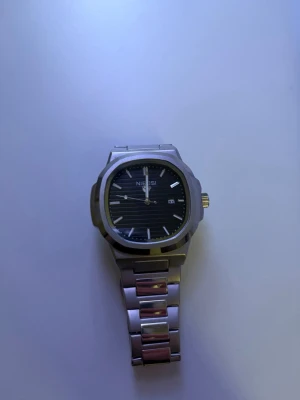 Silverfärgad klocka från Nibosi - ANDVÄND 1 GÅNG. Stilren klocka från Nibosi med silverfärgat armband i metall och svart urtavla med diskreta linjer. Klockan har datumvisning och markerade index. Perfekt accessoar för dig som gillar en klassisk look.