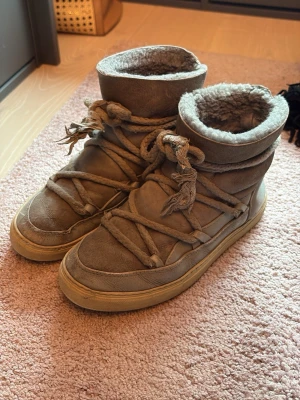 Inuikki skor! Pris kan diskuteras  - Säljer ett par beige Inuikii boots med högt skaft och snörning runt hela skon. Insidan är fodrad med mjuk pälsimitation för extra värme. Yttermaterialet är mocka och sulan är i gummi. Perfekta för kalla dagar och riktigt snygga till vintern.