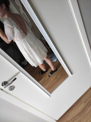 Vit spetsklänning med öppen rygg - Söt vit klänning i spets med öppen rygg och halvlånga ärmar. Klänningen har en rund halsringning framtill och en kort, utsvängd kjol. Perfekt för sommarens alla tillfällen och studenten. Bara provad, kom aldrig till användning på min egna student. 