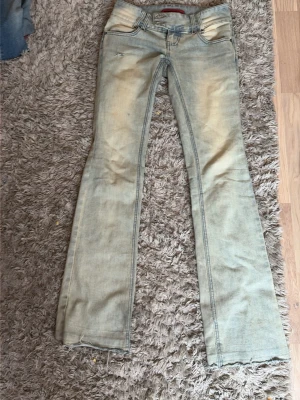 Ljusblå bootcut jeans  - Säljer ett par ljusblå bootcut jeans med slitningar och lätt tvättad look. Jeansen har klassisk femficksdesign och låg midja. Materialet är denim i bomull med stretch för extra komfort. Perfekta för en avslappnad och trendig stil.