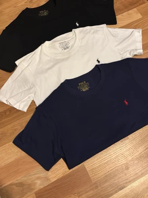 3-pack Polo Ralph Lauren t-shirts - Tre klassiska t-shirts från Polo Ralph Lauren i svart, vitt och marinblått. Alla har rund hals, kort ärm och den ikoniska broderade loggan på bröstet. Perfekta basplagg i mjuk bomull som funkar till allt. Alla är slimfit/ storlek S och de kan köpas var sig själva också! 