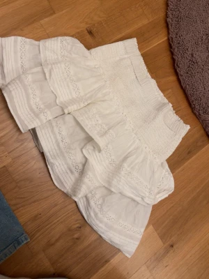 Vit volangkjol med broderi - Supersöt vit kjol med bred smock i midjan som man kan vika ner och flera lager volanger.Köpt för 349kr, säljs inte längre.