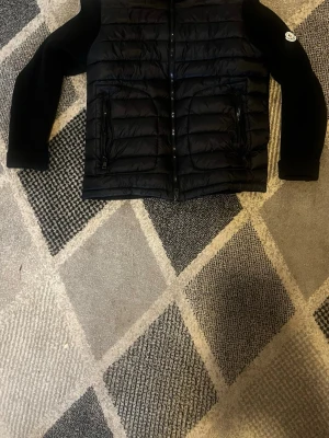 Svart dunjacka - Snygg svart dunjacka  med quiltad front och stickade ärmar. Jackan har hög krage, dragkedja framtill. Perfekt för kalla vinterdagar och riktigt trendig look. Kom privat för mer detaljde bilder svara inom 10 minuter 