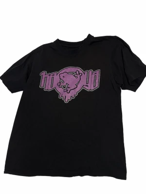 Svart t-shirt med lila grodtryck - Cool svart t-shirt med ett stort lila tryck av en groda och text på bröstet. Klassisk passform och rund halsringning, perfekt för en avslappnad streetwear-look.