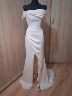 Bal/Fest /Bröllopsklänning  - Passar S-XS.                                             Elegant långklänning i champagnefärg med offshoulder-design och draperad detalj framtill. Klänningen har en slits och ett svepande fall baktill. Perfekt för speciella tillfällen och har en figurnära passform. Finns att köpa och postar på samma dag!💓