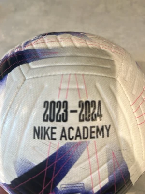 Nike Academy fotboll 2023-2024 - Säljer en Nike Academy fotboll i officiell storlek 4 från säsongen 2023-2024. Bollen är vit med svarta, blå och rosa detaljer samt grafiskt mönster. Perfekt för träning eller match på planen. Tillverkad i slitstarkt material för bra spelkänsla.