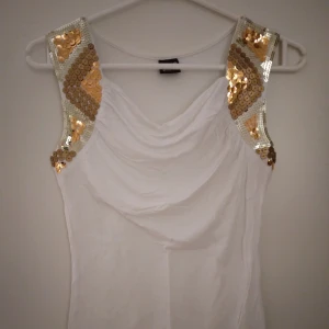 Vit ärmlös topp / linne med snygga glittriga detaljer / paljetter. Strlk: XS-S. Viskos. Gina Tricot. - Vit ärmlös topp / linne med snygga glittriga detaljer / paljetter i guld och silver. Strlk: XS-S. Viskos. Gina Tricot. Felfri. Skyltdockan visar liknande modell och passform.