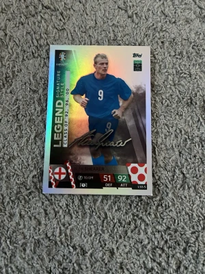 Match Attax Legend fotbollskort England - Säljer ett Match Attax LEGEND Signature fotbollskort från UEFA Euro 2024 med England-tema. Kortet har holografisk yta, visar en spelare i blått matchställ och har tryckt signatur. Perfekt för samlare av fotbollskort och sportmemorabilia.
