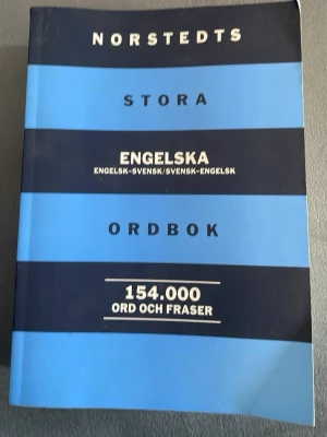 Norstedts stora engelska ordbok - En tjock, blå och svart ordbok från Norstedts med titeln 'Stora engelska ordbok'. Innehåller 154 000 ord och fraser, både engelska-svenska och svenska-engelska. Perfekt för dig som pluggar språk eller vill förbättra din engelska.