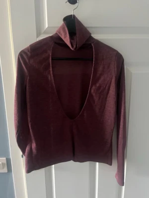 Vinröd polotopp med öppen rygg - Trendig vinröd polotopp med lång ärm och öppen rygg. Toppens material har en lätt glansig finish och känns mjuk mot huden. Perfekt för dig som vill sticka ut med en unik och snygg topp.