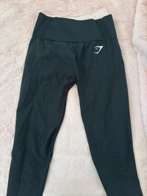 Svarta seamless leggings från Gymshark - Snygga svarta seamless leggings från Gymshark med hög midja och diskret mönstrad struktur längs benen. Stretchigt material som sitter tajt och bekvämt. Perfekta för träning eller chill. Gymshark-logga på ena höften.
