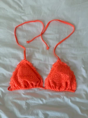 Orange trekantsbikini med spetsdetaljer - Snygg orange trekantsbikini med virkade spetsdetaljer och knyt i nacken. Perfekt för stranden eller poolen, med en fräsch och ungdomlig look. Bikinin har en klassisk trekantsform och tunna band för enkel justering.