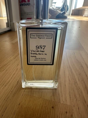 The Essence Vault 987 parfym 100ml - Parfymflaska från The Essence Vault, doft 987 inspirerad av Valentino Donna Born in Roma. Flaskan är genomskinlig med silverfärgad spraykork och rymmer 100 ml Eau de Parfum. Modern och stilren design i glas.