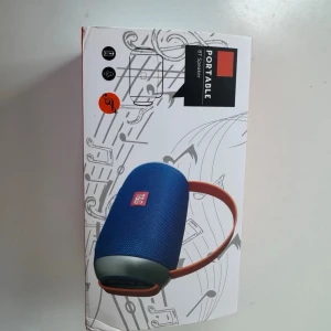 Blå trådlös högtalare med handtag - Snygg blå trådlös högtalare från T&G med rundad form och orange bärhandtag. Högtalaren har tygklädd yta och detaljer i plast. Perfekt för att ta med sig musiken överallt tack vare den portabla designen.