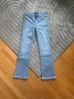 Ljusblå bootcut jeans från Lee - Säljer ett par ljusblå bootcut jeans från Lee med klassisk femficksdesign och normal midja. Jeansen har en snygg tvätt och är tillverkade i mjuk denim med lite stretch för extra komfort. Perfekta för en avslappnad och trendig look.