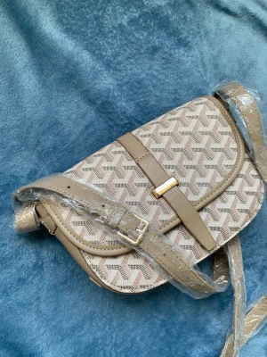 Beige axelväska med mönster - Snygg beige axelväska med geometriskt mönster och justerbar axelrem. Väskan har lock med magnetlås.