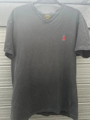 2  t-shirts från Polo Ralph Lauren - Svart och grå t-shirts från Polo Ralph Lauren med klassisk broderad logga på bröstet. Och nere vid kanten på den andra  T-shirten är kortärmad och tillverkad i mjuk bomull, perfekt för en stilren och avslappnad look. Storlek M på båda