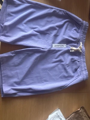 Ljuslila Manchester shorts från Novant - Säljer ett par ljuslila shorts från Novant med elastisk midja och vit snörning. Shortsen har en avslappnad passform och passar bra för medium/large.