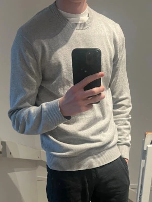 Ljusgrå stickad tröja Massimo Dutti - Snygg ljusgrå stickad tröja från Massimo Dutti. Tröjan har rund halsringning, ribbade muddar och en clean, minimalistisk look som passar till allt. Perfekt för dig som gillar stilrena och bekväma plagg.
