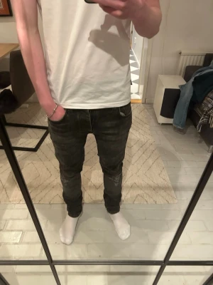 Svarta nudiejeans slim fit  - Säljer ett par svarta slim fit jeans från nudie jeans med klassisk femficksdesign och diskreta slitningar. Jeansen har en smal passform och normal midja, perfekta för en trendig och avslappnad stil i storlek 29/32. Materialet är stretchigt för extra komfort. 